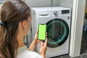 Young woman using mobile phone control via wi-fi and app for washing machine in home. Homesmart app, chroma key green screen. High quality photo