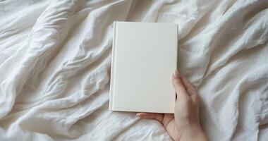 Close-up mockup of woman hands holding a blank white book. Ideal for book cover design, branding, and product display. Minimalist and cozy scene photo