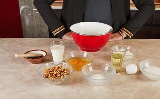 A kitchen table with a red mixing bowl and various ingredients, including eggs, milk, and walnuts, ready for muffin preparation. photo