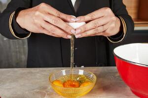 A person cracks fresh eggs into a glass bowl, preparing ingredients for a homemade baking recipe in a cozy kitchen setting. photo