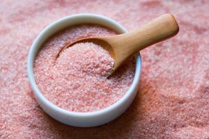 Himalayan pink salt in a bowl and wooden spoon on pink salt background photo
