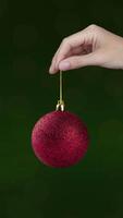 Hand shows a Christmas tree red ball with 2025 that rotates. Green background vertical banner motion animation close up video