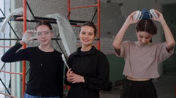 Three young women, working as builders and interior designers, pose for camera while standing on construction site, smiling and taking off their protective gear as their day comes to an end. video