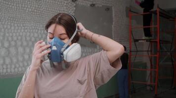 Attractive young woman puts on respirator to protect her health while preparing to work at construction site where there are harmful substances and dust in air that could damage her lungs. video