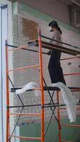 Woman stands confidently on scaffold and paints the upper part of wall in golden color using a spray can with compressed air and paint. video