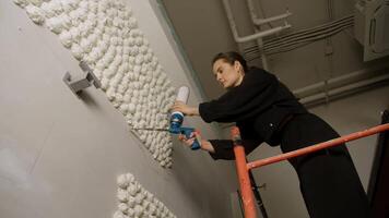 Young and attractive woman is standing on scaffold, creating unique interior design solution. She is creating a bas-relief on wall. video