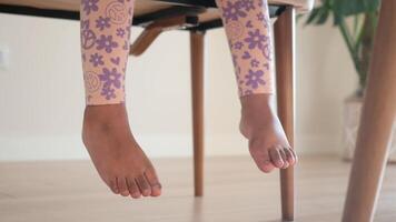 Childs small feet playfully dangling below the table in colorful leggings video