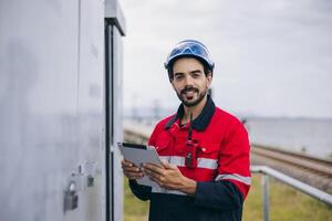 man in a red and black safety suit is holding a tablet and smiling photo