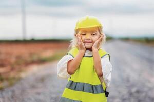 young girl wearing a yellow vest and a hard hat is standing on a road photo