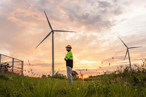 man stands in a field next to two wind turbines photo