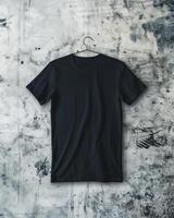 A plain black t-shirt is laid flat on a textured, grungy concrete background, showcasing its simple design and fabric texture. photo