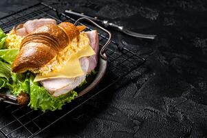 Breakfast croissant sandwich with scrambled eggs, cheese and ham. Black background. Top view. Copy space photo