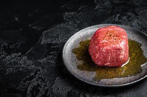 Fillet Mignon prime beef steak, raw dry aged marble meat with herbs and spices ready for cooking. Black background. Top view. Space for text photo