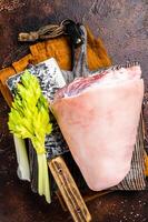 Fresh Raw pork shank knuckle on a butcher board with herbs for cooking. Dark background. Top view photo