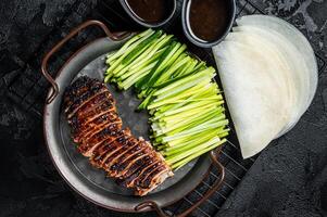 Peking Duck served with cucumber, green onions, and roasted wheaten chinese pancakes with sauce Hoysin. Black background. Top view photo