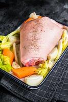 Cooking of Schweinshaxe from Raw pork shank knuckle with vegetables and herbs. Black background. Top view photo