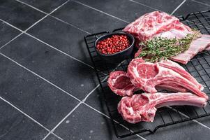 Fresh Raw lamb meat chop steaks on kitchen table with spices and herbs. Black background. Top view. Copy space photo