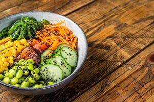 Poke bowl with fresh Salmon fish, rice, seaweed, edamame, cucumber and black sesame. Wooden background. Top view. Copy space photo