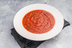 Tomato soup with thyme in plate. grey background. top view photo
