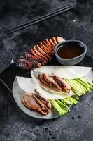 Traditional served Peking Duck with cucumber, green onion, in wheaten chinese pancakes. Black background. Top view photo
