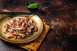 Asian appetizer pig pork ears with sesame seeds, green onion and spicy sauce. Dark background. Top view. Copy space photo