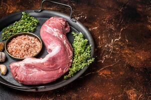 Uncooked Raw pork tenderloin fillet meat on a kitchet tray with thyme, garlic and sea salt. Dark background. Top view. Copy space photo