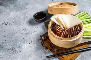 Peking Duck in bamboo steamer served with cucumber, green onion, and wheaten chinese pancakes and sauce Hoysin. Gray background. Top view. Copy space photo