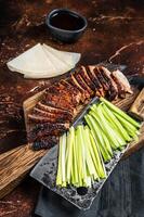 Sliced Peking Duck served with cucumber, green onion, and wheaten chinese pancakes on a meat cleaver. Dark background. Top view photo