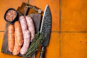 Fresh Raw Bratwurst and Chorizo meat sausages on wooden board. Orange background. Top view. Copy space photo