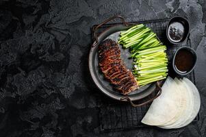 Peking Duck served with cucumber, green onions, and roasted wheaten chinese pancakes with sauce Hoysin. Black background. Top view. Copy space photo