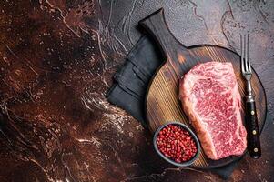 Uncooked Raw striploin or club steak on wooden board with thyme. Dark background. Top view. Copy space photo