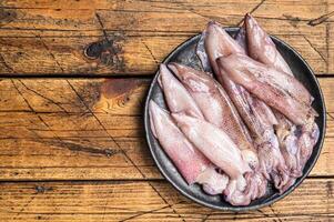 Raw squid, fresh calamari in a plate. Wooden background. Top view. Copy space photo