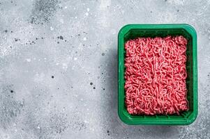 Raw Minced Meat in a Plastic Container, ground beef. Gray background. Top view. Space for text photo