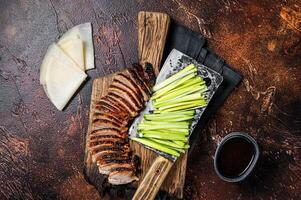 Sliced Peking Duck served with cucumber, green onion, and wheaten chinese pancakes on a meat cleaver. Dark background. Top view photo
