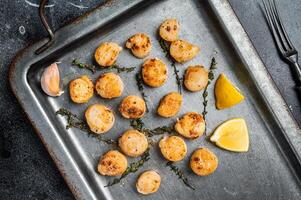 Scallops poached in a butter and garlic Sauce in a steel tray with thyme. Black background. Top view photo