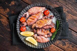 Grilled squid, calamary in a plate with herbs. Wooden background. Top view photo