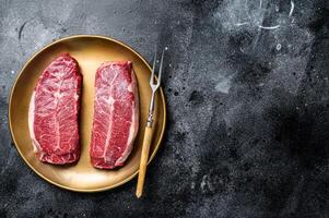 Raw Shoulder Top Blade beef meat steaks on a plate. Black background. Top View. Copy space photo