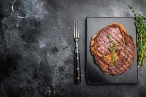 Rib eye steak with herbs on marble board, grilled prime beef meat. black background. top view photo