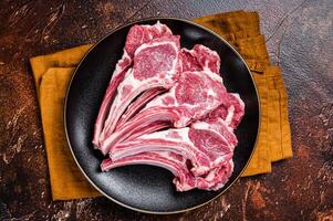 Raw lamb chops, fresh mutton meat cutlets on a ribs. Dark background. Top view photo