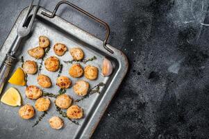 Scallops poached in a butter and garlic Sauce in a steel tray with thyme. Black background. Top view. Copy space photo