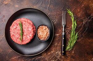 Raw veal and beef minced meat cutlets for burgers with herbs on plate. brown background. top view photo