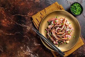 Asian appetizer pig pork ears with sesame seeds, green onion and spicy sauce. Dark background. Top view. Copy space photo