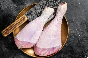Fresh turkey legs Drumsticks, raw Poultry meat with butcher cleaver. Black background. Top view photo