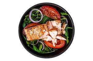 Grilled salmon fish fillet steak with fresh salad arugula, avocado and tomato in a pan. Isolated, white background. Top view. photo