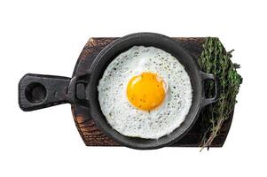 Salted and spiced fried egg in pan with tomatoes, thyme and bacon. Isolated on white background photo
