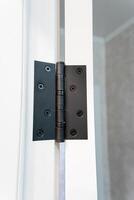 This is a close up image featuring a black door hinge mounted on a white door photo