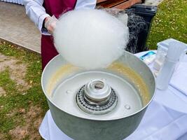A skilled individual expertly operates a machine that produces delicious cotton candy, skillfully spinning it into sweet, fluffy clouds that are truly delightful and enjoyable to eat photo