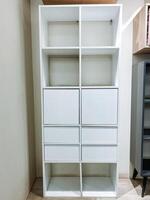 In a cozy room, there stands a lovely white shelf, which features both drawers and doors, offering ample storage space, enhancing the overall decor, and serving multiple diverse functions photo