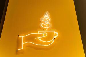 An illuminated neon sign depicts a hand gracefully holding a cup of coffee photo