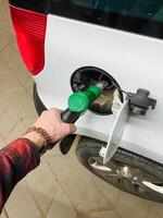 A person is currently in the act of pumping gas into a white vehicle, which is parked at a gas station, ensuring that it receives the fuel needed for its operation and travel photo